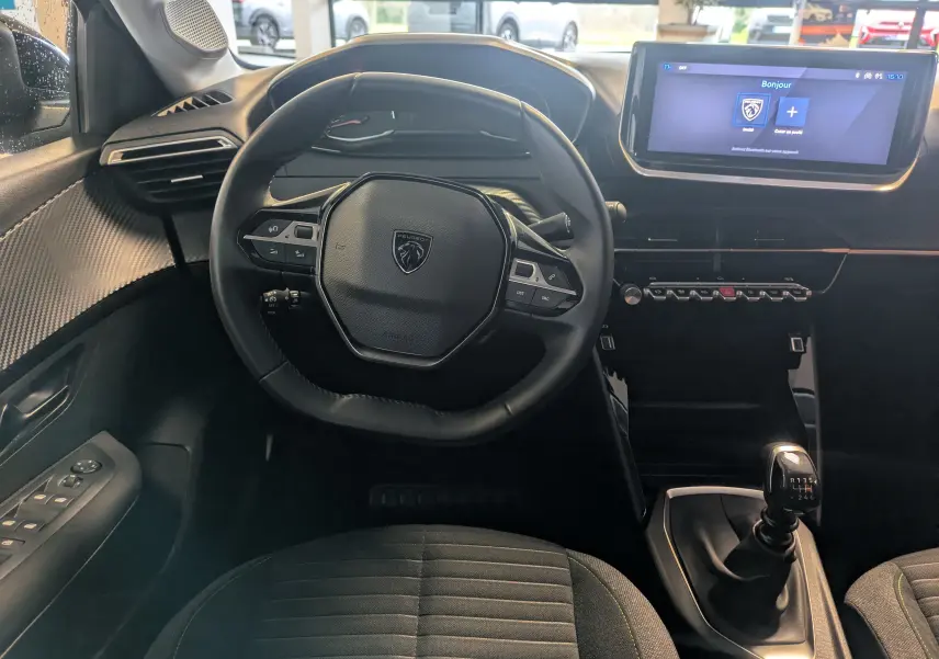 Vue intérieure centrée sur le volant cuir et la console avec écran tactile du Peugeot 208 noir Perla 2024.