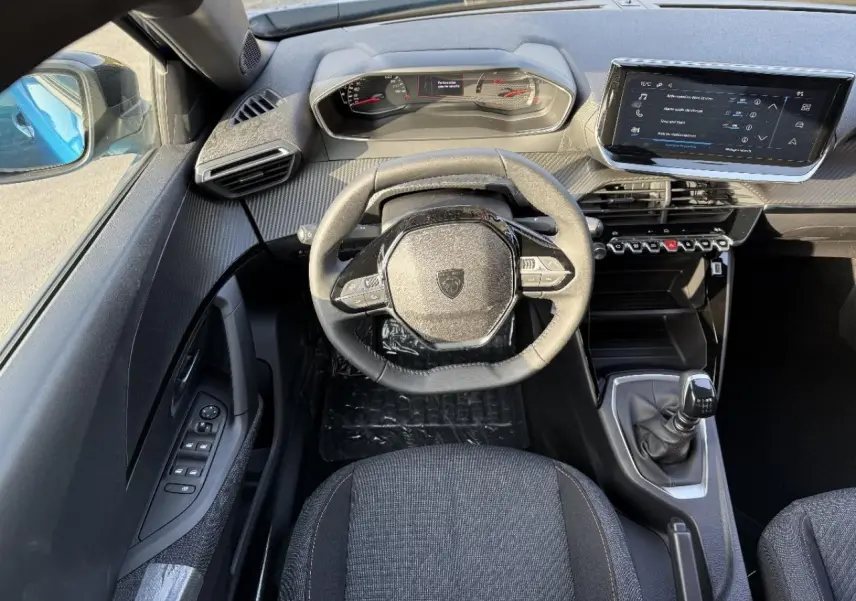 Vue intérieure du poste de conduite du Peugeot 2008 2025, volant compact, écran tactile et levier de vitesse manuel visibles.
