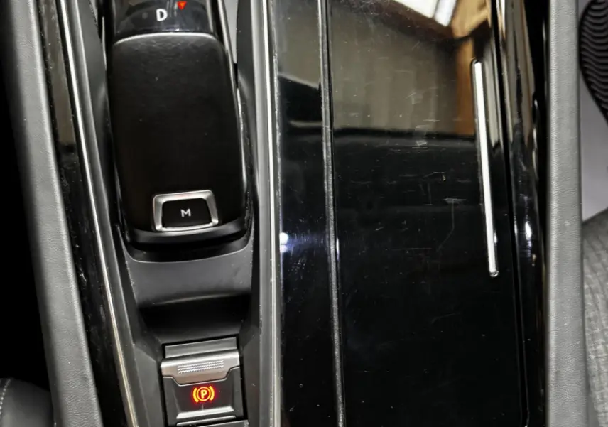 Gros plan sur la console centrale noire brillante de la Peugeot 508, avec levier de vitesse automatique et bouton frein à main électronique allumé.