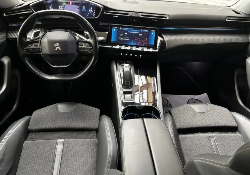 Vue intérieure avant de la Peugeot 508 gris foncé, mettant en valeur le volant cuir, l'écran tactile et la console centrale brillante.