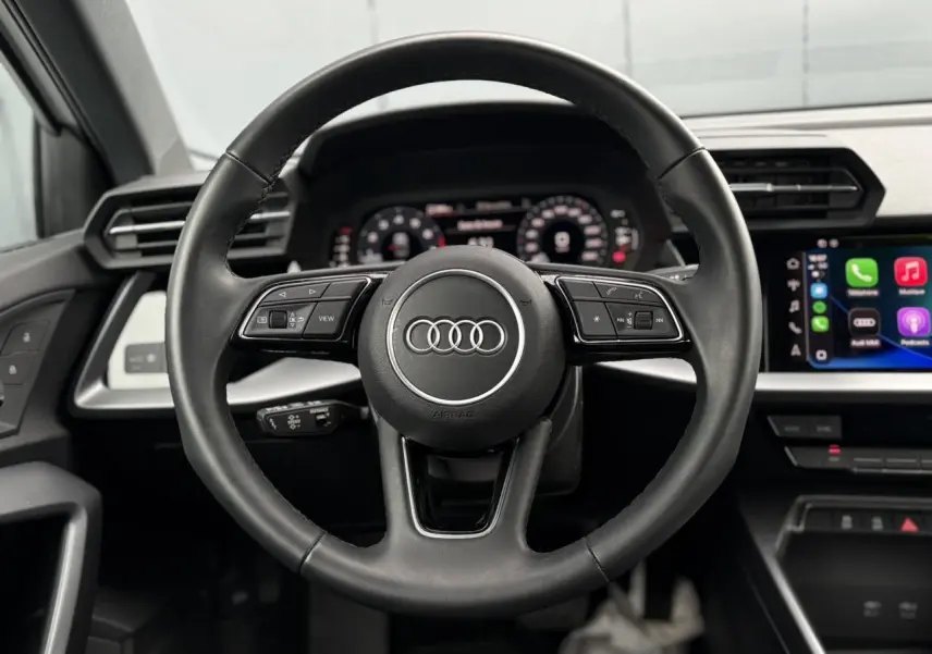 Vue rapprochée du volant cuir noir multifonctions de l'Audi A3 Berline 2024 avec tableau de bord digital et écran central.