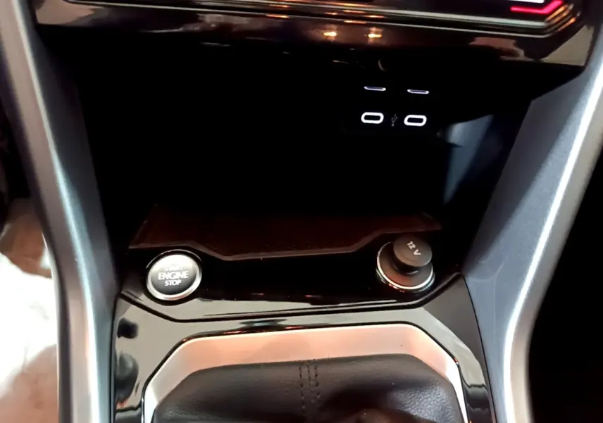 Gros plan sur la console centrale du Volkswagen T-Roc gris foncé, montrant bouton start/stop et prise 12V.