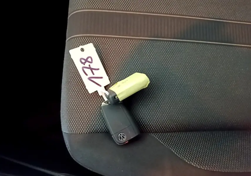 Clé noire Volkswagen posée sur la banquette arrière en tissu gris foncé à motifs, vue en plongée rapprochée.