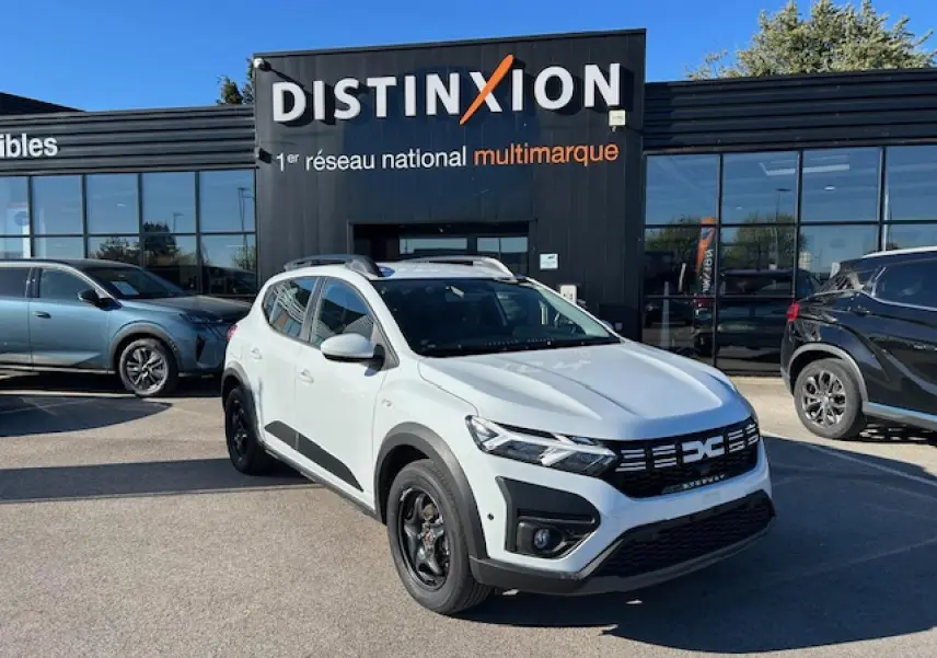 Dacia Sandero Stepway blanc arctique vue 3/4 avant avec calandre noire et barres de toit noires devant un showroom.