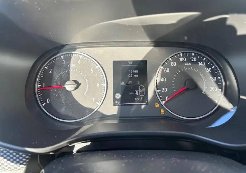 Vue rapprochée du tableau de bord numérique et compteurs analogiques de la Dacia Sandero blanche, affichant la vitesse et le régime moteur.