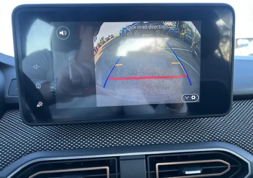 Écran tactile intérieur affichant la caméra de recul d’une Dacia Sandero Stepway blanche, avec tableau de bord texturé noir.