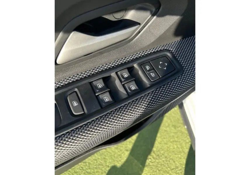 Gros plan sur les commandes des vitres électriques côté conducteur avec insert gris texturé, portière blanche visible en arrière-plan.