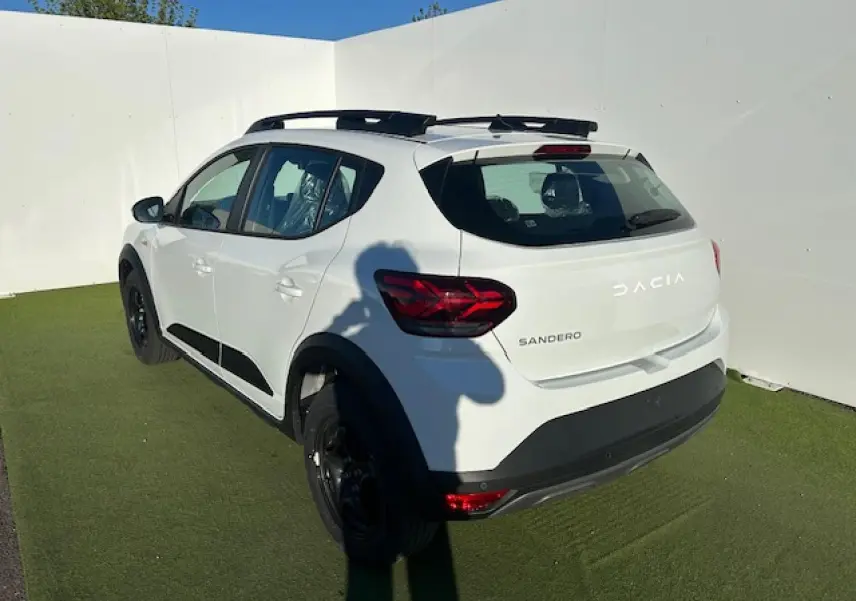 Vue 3/4 arrière droite d'une Dacia Sandero Stepway blanche avec barres de toit noires et feux arrière LED en Y.