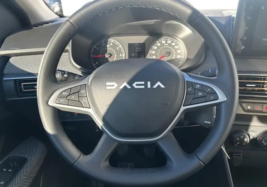 Vue rapprochée du volant noir de la Dacia Sandero Stepway 2025 avec commandes intégrées et tableau de bord numérique.