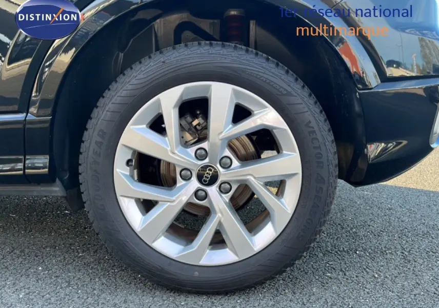 Gros plan sur la roue avant droite d'un Audi Q2 noir mito metal avec jante argentée à plusieurs branches.