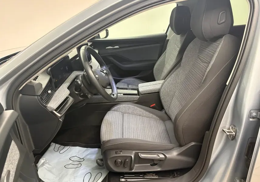 Vue intérieure côté conducteur de la Skoda Superb Combi 2025 gris argent, sièges tissu gris et tableau de bord moderne.