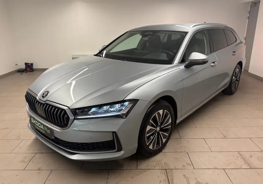 Skoda Superb Combi gris argent en 3/4 avant droit, avec calandre noire et jantes alliage distinctives.