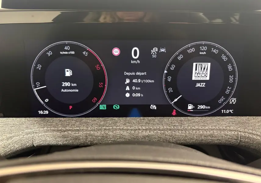 Tableau de bord numérique du Skoda Superb Combi gris argent 2025, affichant vitesse, autonomie et radio Jazz en vue frontale.