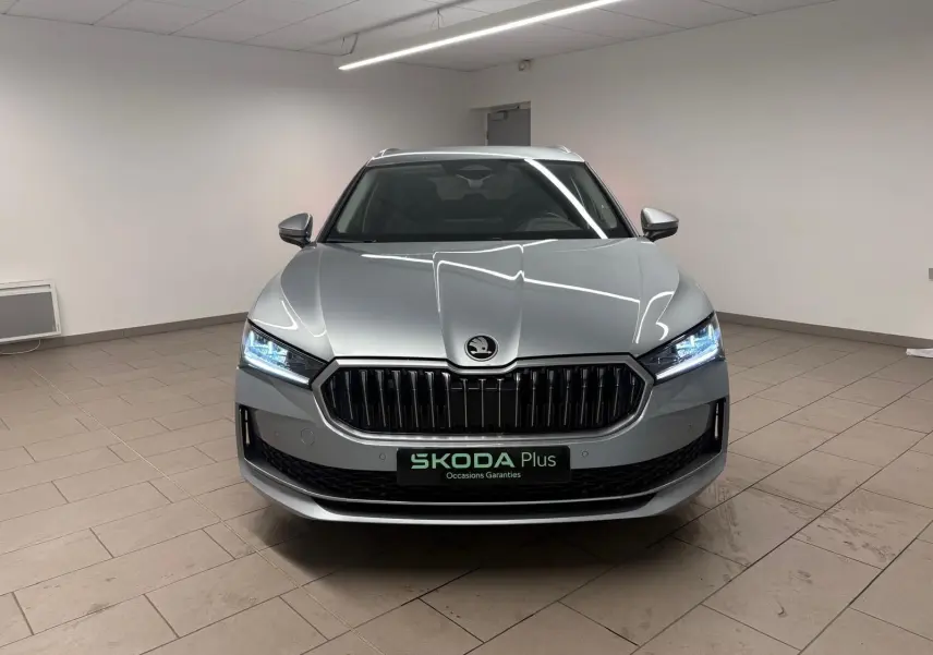 Vue frontale d'une Skoda Superb Combi gris argent 2025 avec calandre noire et phares LED allumés en intérieur.
