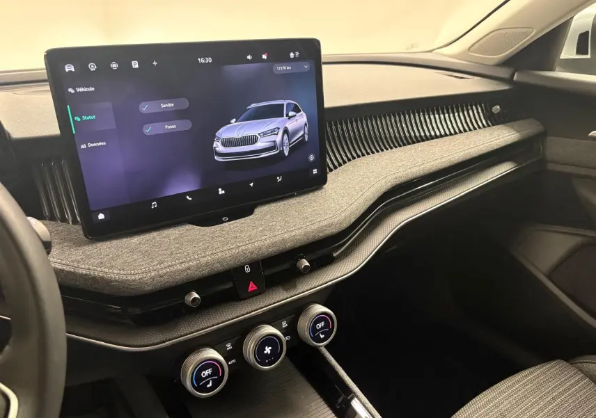 Vue intérieure côté passager du tableau de bord gris clair du Skoda Superb Combi 2025 avec écran tactile central et commandes climatisation.