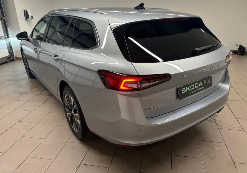 Vue 3/4 arrière droite d'une Skoda Superb Combi gris argent avec feux arrière allumés dans un garage.