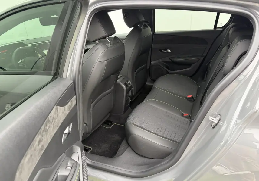Vue côté gauche arrière de l’habitacle gris d’une Peugeot 308 III hybride avec sièges noirs et surpiqûres vert Adamite.