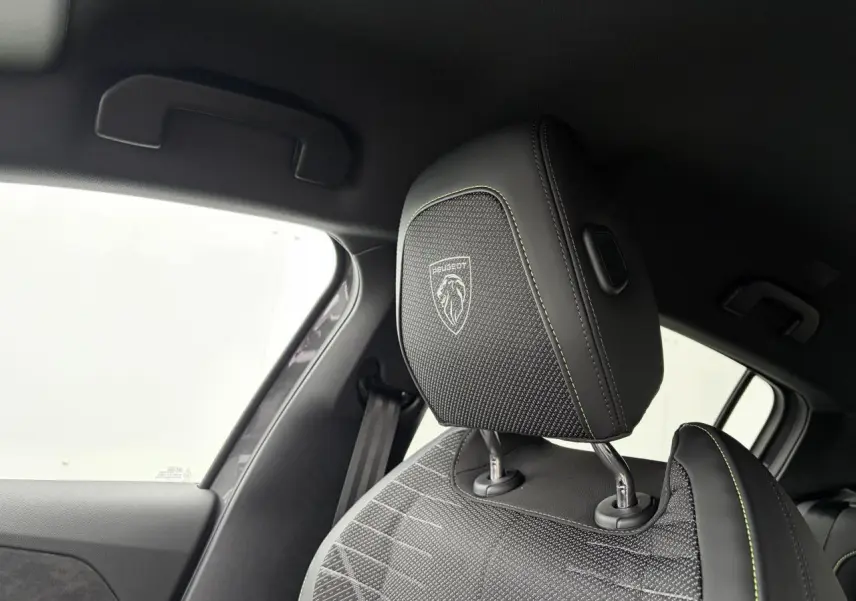 Gros plan sur l'appui-tête avant droit noir avec surpiqûres vert Adamite et logo Peugeot dans l'habitacle.