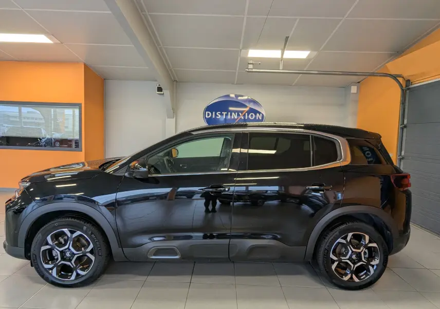 Profil côté gauche d'un Citroën C5 Aircross noir 2024 avec jantes alliage 18 pouces bicolores en intérieur showroom.