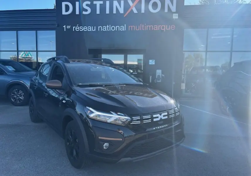 Vue 3/4 avant d'une Dacia Sandero Stepway noire nacrée avec calandre et rétroviseurs brun cuivré, stationnée devant un bâtiment.