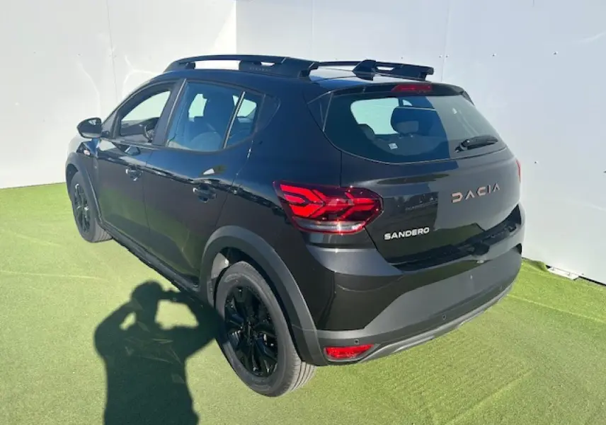 Vue 3/4 arrière droite d'une Dacia Sandero III Stepway noire nacrée avec jantes noires et barres de toit.