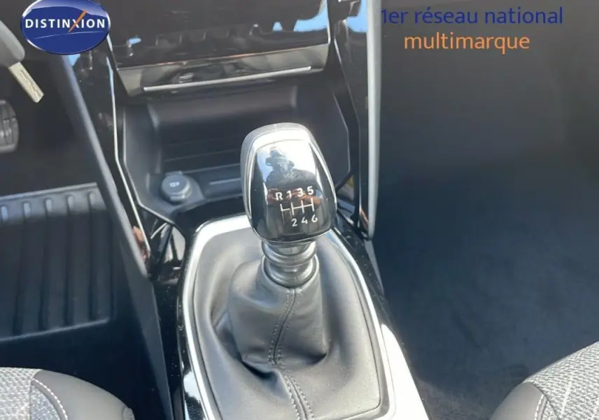 Gros plan sur le levier de vitesse manuel noir du Peugeot 2008 gris, avec console centrale brillante en arrière-plan.