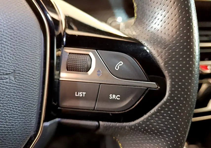 Gros plan sur les commandes gauche du volant en cuir perforé du Peugeot 208 GT Line rouge, boutons téléphonie et navigation.