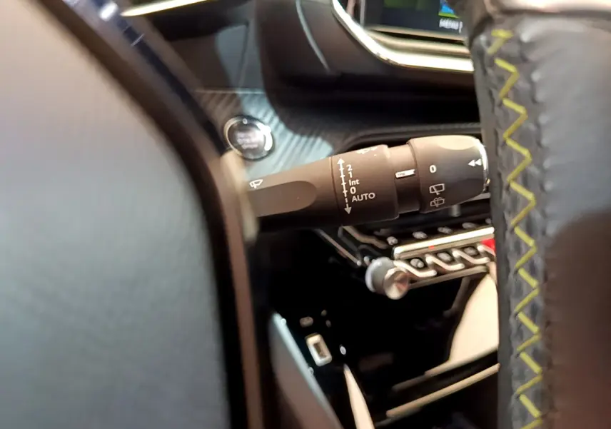 Gros plan sur la manette d’essuie-glace à gauche du volant cuir noir avec surpiqûres jaunes dans une Peugeot 208 rouge.