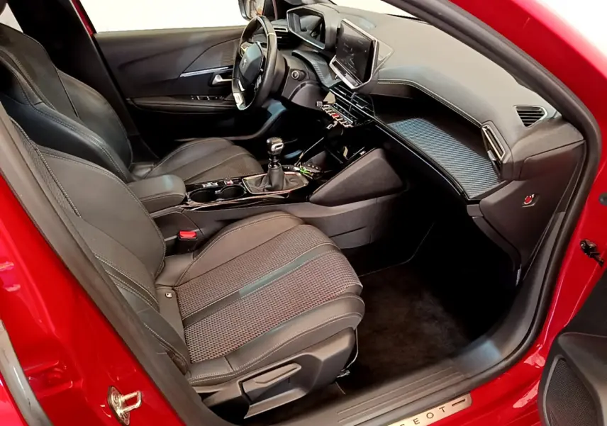 Intérieur côté conducteur d'une Peugeot 208 rouge, montrant sièges en cuir, volant multifonctions et tableau de bord moderne.