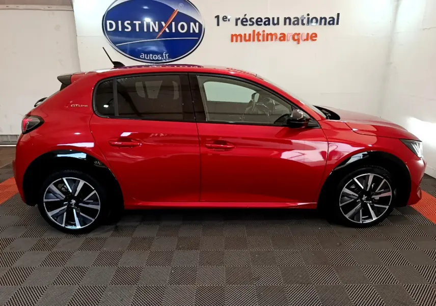 Profil côté gauche d'une Peugeot 208 GT Line rouge 2020 avec jantes alliage et vitres teintées en intérieur showroom.