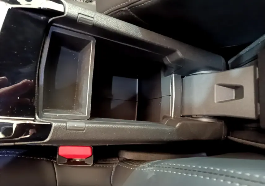 Vue plongeante sur le rangement central noir ouvert de la Peugeot 208 GT Line rouge, avec bouton de frein à main visible.