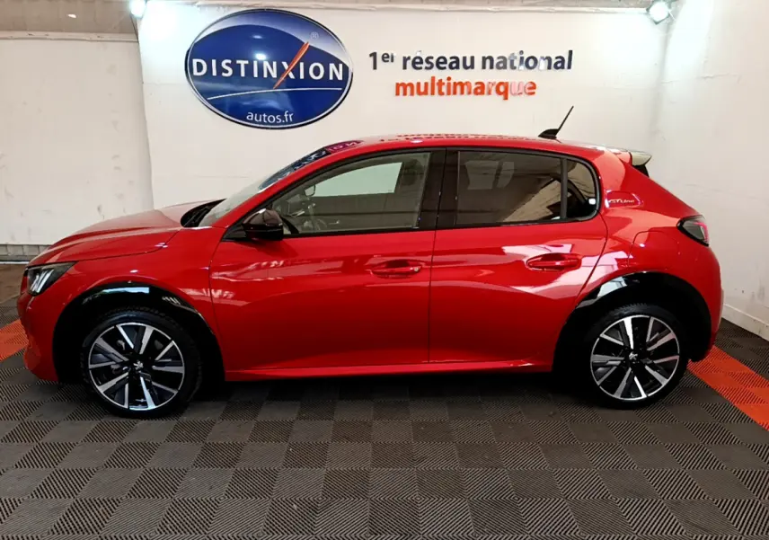 Profil côté gauche d'une Peugeot 208 GT Line rouge de 2020, avec jantes alliage et vitres teintées en intérieur showroom.