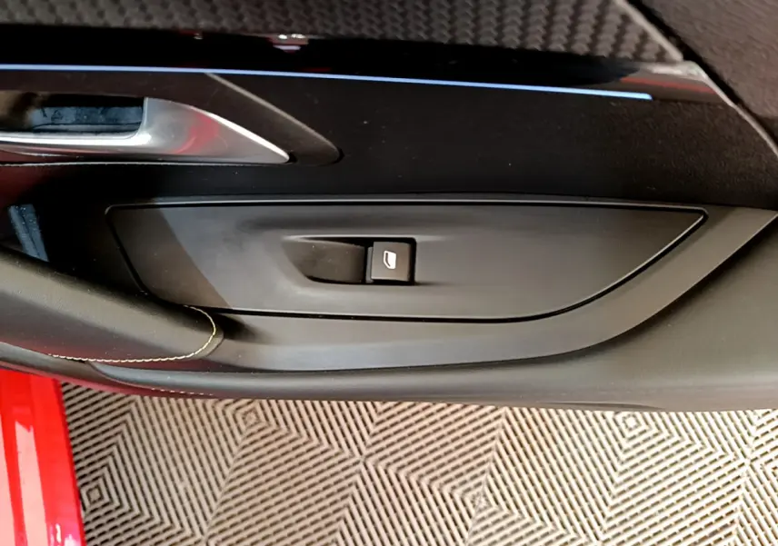 Gros plan sur la commande de lève-vitre côté gauche de la porte intérieure d’une Peugeot 208 rouge.
