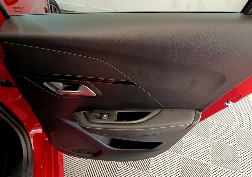 Vue rapprochée de la porte avant gauche rouge d'une Peugeot 208 GT Line avec garniture noire et surpiqûres jaunes.
