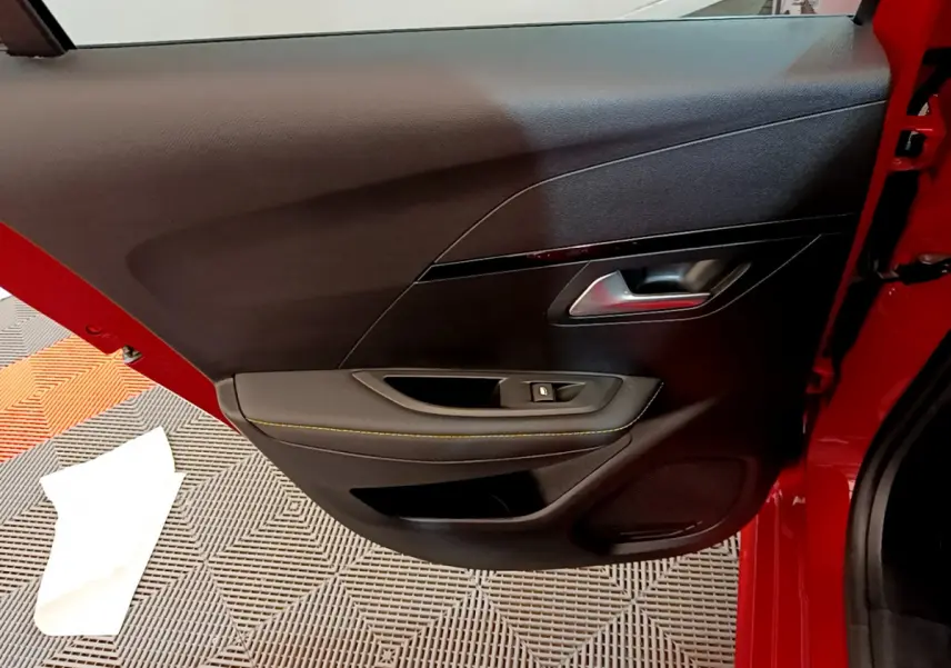 Vue intérieure de la porte arrière gauche rouge de la Peugeot 208 GT Line avec poignée argentée et bouton de vitre électrique.