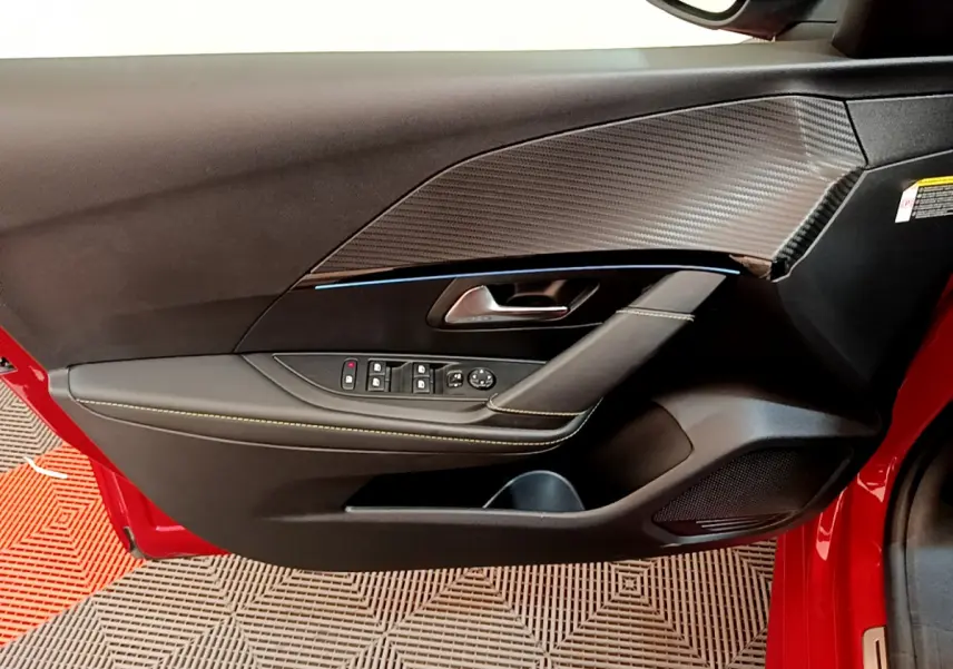 Vue rapprochée de la porte avant gauche rouge d'une Peugeot 208 GT Line avec garniture noire et surpiqûres contrastées.