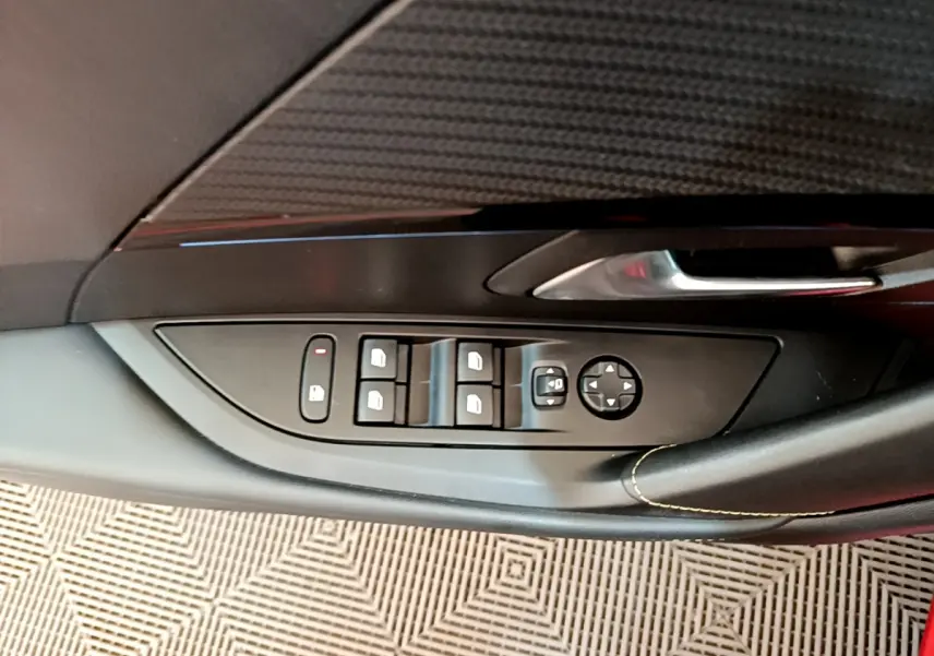 Gros plan sur la commande des vitres et rétroviseurs côté conducteur d'une Peugeot 208 rouge, finition GT Line.