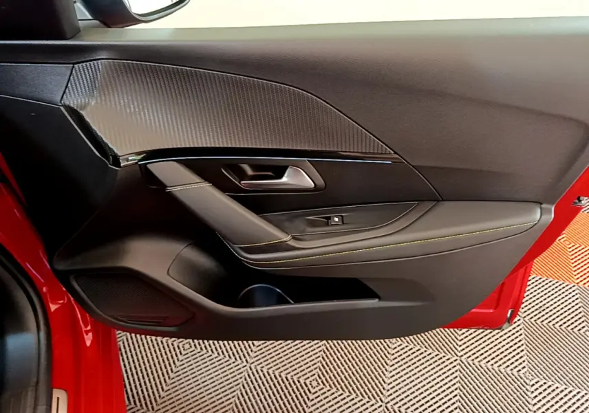 Vue rapprochée de la porte avant gauche rouge d'une Peugeot 208 GT Line avec garniture noire et surpiqûres jaunes.