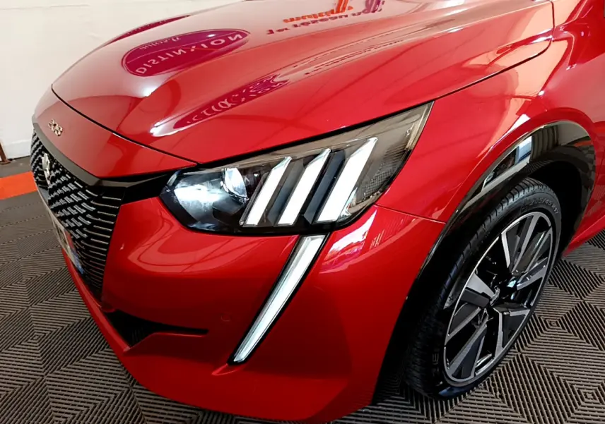 Gros plan sur l'avant droit de la Peugeot 208 GT Line rouge, mettant en valeur ses phares LED et sa calandre distinctive.
