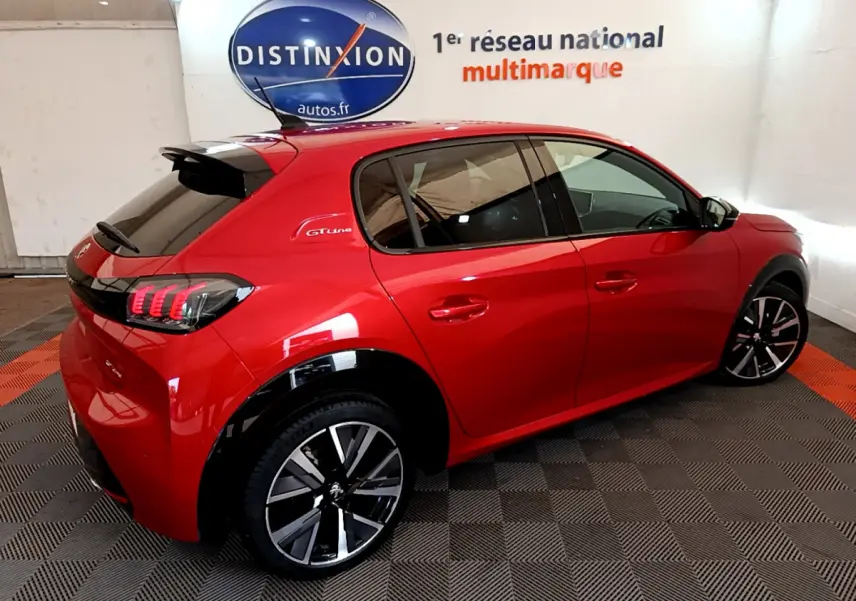 Vue 3/4 arrière droite d'une Peugeot 208 GT Line rouge avec jantes alliage et vitres teintées dans un showroom