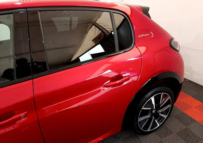 Vue côté droit arrière d'une Peugeot 208 GT Line rouge avec jante alliage et logo GT Line sur l'aile arrière.