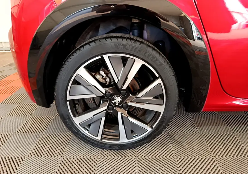 Gros plan sur la roue avant gauche de la Peugeot 208 rouge, mettant en valeur la jante alliage au design moderne.