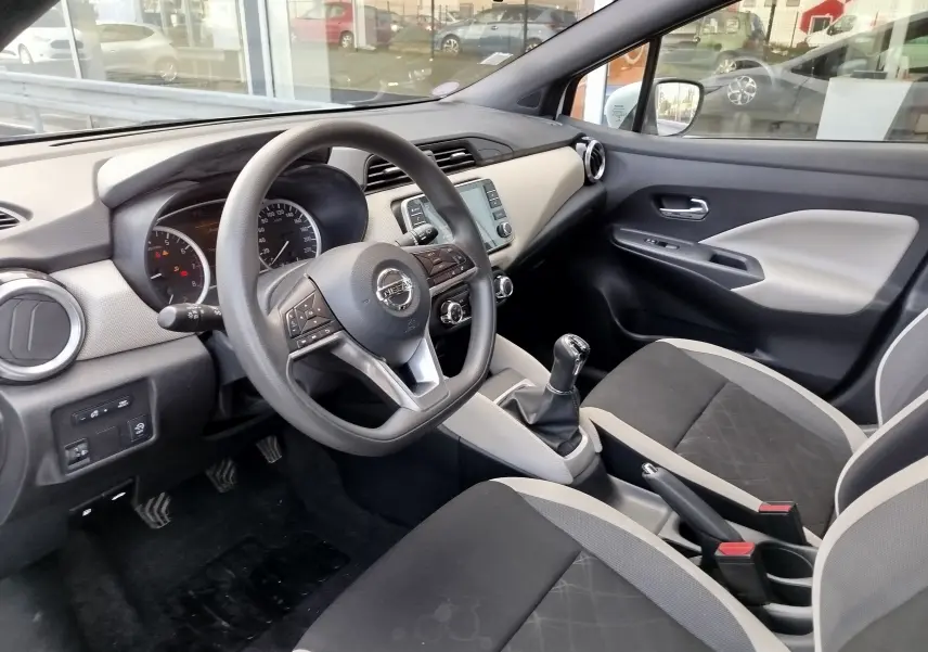 Vue intérieure côté conducteur de la Nissan Micra blanche 2019 avec volant multifonction et sellerie bicolore gris noir.