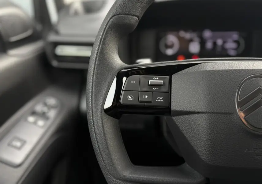 Gros plan sur le volant multifonctions noir du Citroën Berlingo blanc Icy, avec commandes de régulateur à gauche.