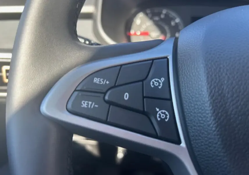 Gros plan sur les commandes du régulateur de vitesse au volant noir du Dacia Sandero III Stepway beige Safari.