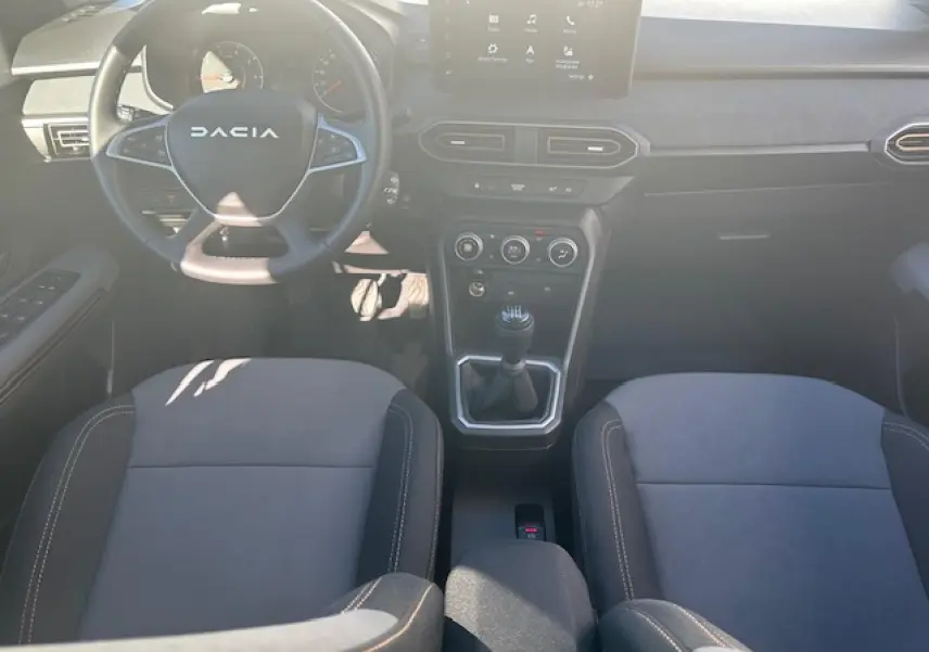 Vue intérieure avant de la Dacia Sandero III Stepway, tableau de bord noir avec écran tactile et volant multifonction.