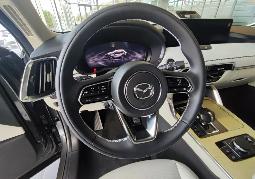 Vue intérieure centrée sur le volant cuir noir et tableau de bord clair du Mazda CX-80 hybride rechargeable 2024.