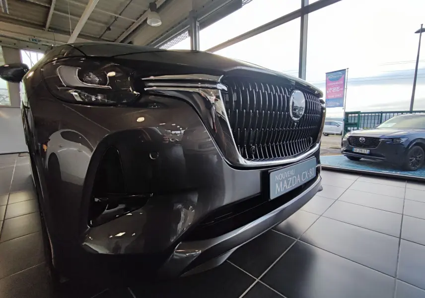 Vue 3/4 avant gauche du Mazda CX-80 gris foncé avec sa calandre imposante et ses phares LED dans un showroom.