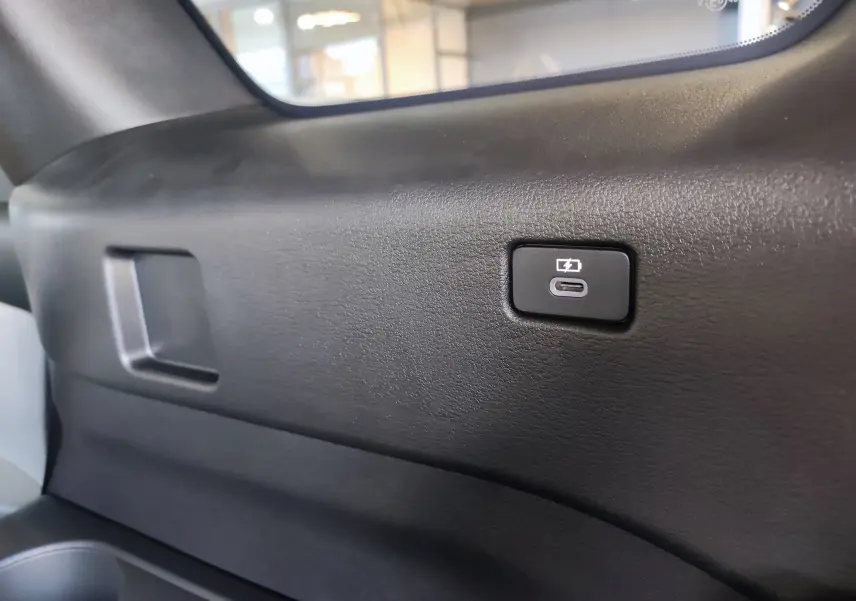 Bouton de recharge USB-C visible sur la garniture intérieure noire du coffre du Mazda CX-80 hybride rechargeable 2024.