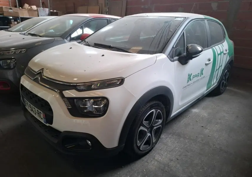 Vue 3/4 avant d'une Citroën C3 blanche avec décor vert et jantes noires dans un garage sombre